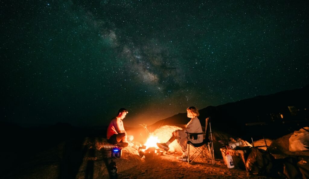 campers sitting around a camp fire under a starry night sky